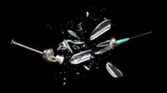 photo of a syringe for administering vaccines being smashed against a black backdrop