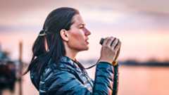 Woman holding one of the best compact binoculars against a watery sunset