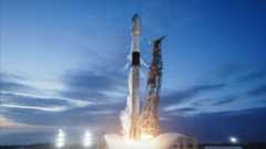 a white and black rocket ignites its engines to lift off from a launch pad under a mostly clear dusk blue sky