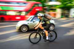 A man in lycra on a black bike cycles past a green car in London