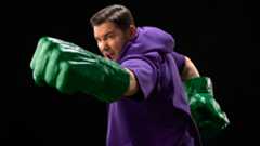 A man yells while punching with giant green Hulk Fists