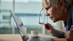 Woman looks at laptop on desk with glasses taken off