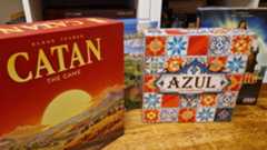 Catan, Azul, Carcassonne, and Pandemic boxes on a wooden table in front of bookshelves
