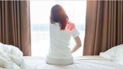 The image shows a woman sitting up in bed and clutching her shoulder in pain