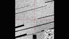 A gray grainy image with a red cross hair in the middle zooming in on a black dot against the grains
