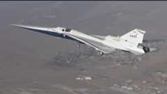 A small white plane flies above the desert
