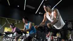 Young people riding stationary bike during indoor cycling class in gym.