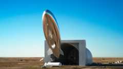 A silvery blimp shape satellite seems to float above the desert of New Mexico