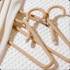 Two cream-colored rope hangers lay on a white textured fabric with a draped piece of apparel covering them.