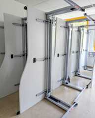 Dieser Alternativtext wurde KI-generiert: Mehrere weiße Paneele sind an Metallschienen montiert und stehen auf Rädern. Die Konstruktion wirkt wie eine Art Raumteiler oder mobile Wand.