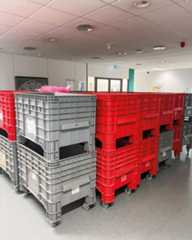 Dieser Alternativtext wurde KI-generiert: Mehrere übereinander gestapelte Plastikkisten in verschiedenen Farben stehen in einem hellen Raum. Die Kisten stehen auf Rollen und sind teilweise mit Gegenständen befüllt.