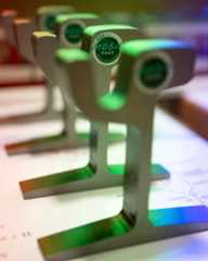 Dieser Alternativtext wurde KI-generiert: Nahaufnahme einer metallischen Struktur mit grünen, runden Elementen. Im Hintergrund ist ein farbiges, abstraktes Muster zu sehen.