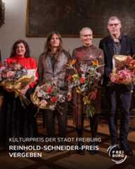 Dieser Alternativtext wurde KI-generiert: Schwarz-weißes Foto von vier Personen, die Blumensträuße halten. Im Hintergrund hängt ein großes Gemälde, und der Text