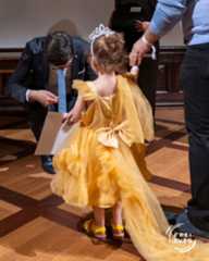 Dieser Alternativtext wurde KI-generiert: Eine Person hilft einer anderen Person beim Anpassen der Kleidung. Das Bild zeigt eine Innenansicht mit einer hellen Holzfläche.