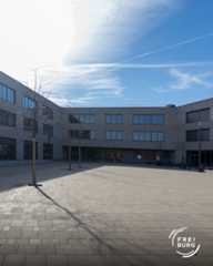 Dieser Alternativtext wurde KI-generiert: Ein moderner Gebäudekomplex mit einem gepflasterten Innenhof. Der Himmel ist leicht bewölkt und hellblau.