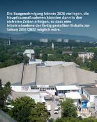 Dieser Alternativtext wurde KI-generiert: Ein Luftbild zeigt eine Stadtlandschaft mit Gebäuden unterschiedlicher Höhe und einem großen, hellen Bauwerk im Vordergrund. Im Hintergrund erstrecken sich grüne Hügel und Berge.