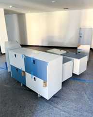 Dieser Alternativtext wurde KI-generiert: Ein hell erleuchteter Raum mit mehreren Schrankelementen auf Rollen. Die Schränke sind blau und weiß und mit Klebeband gesichert.