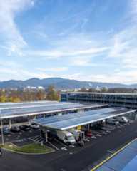 Dieser Alternativtext wurde KI-generiert: Eine Aufnahme von einem Parkplatz mit vielen Solarzellen auf dem Dach. Im Hintergrund sind Gebäude und Berge zu sehen.