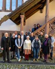 Dieser Alternativtext wurde KI-generiert: Eine Gruppe von Menschen steht vor einem Gebäude mit einem Treppenhaus. Das Foto wurde im Freien aufgenommen und zeigt eine Pflasterstein-Unterlage.