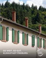 Dieser Alternativtext wurde KI-generiert: Ein Gebäude mit einem Ziegeldach und grünen Fensterläden ist vor einem dichten, grünen Wald zu sehen. Der Hintergrund ist unscharf und das Bild hat ein helles Farbschema.