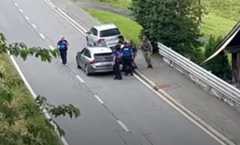 Policiers arrêtant un individu sur une route avec deux voitures garées, entourés de végétation.