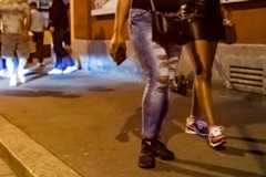 Deux personnes marchant le long de la Langstrasse à Zurich, l’une portant un jean déchiré et l’autre une jupe en cuir, la nuit.