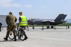 Un avion F-35A exposé sur le tarmac avec deux hommes en uniforme militaire, l’un à vélo, lors d’un événement en Suisse.
