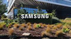 A large 'SAMSUNG' sign is prominently displayed in front of a modern Samsung office building surrounded by landscaped