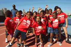 A group of young students - mainly BIPOC students - smiling and waving hands to the camera in a New York City park.