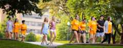 Students walk through a lush campus in early spring wearing bright orange shirts