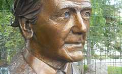 A bronze-coloured bust on top of a black stone.