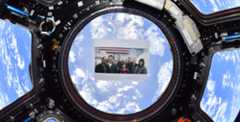A photograph of the Lightyear filmmakers is placed on a window of the International Space Station with planet earth in clear view behind it.