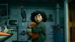 In a still from Disney and Pixar’s Hoppers, Mabel, voiced by Piper Curda, stands in profile, clutching a lifelike robotic beaver. She wears a green fleece-like jacket and has a startled expression of her face. A row of gray file cabinets, monitors, and a half-built robotic bird-like creature and rabbit are seen in the background.