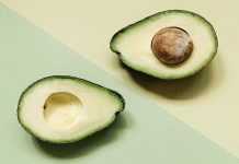 A sliced avocado on a pastel green and yellow background, showcasing its seed and texture.