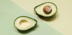 A sliced avocado on a pastel green and yellow background, showcasing its seed and texture.