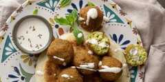 A plate of golden falafel drizzled with tahini, served with mint garnish and creamy dip