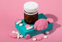 A pill bottle, pink brain model, and scattered pills on a colorful pink backdrop.