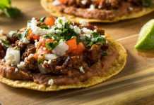 Crispy tostada topped with fresh lettuce, diced tomatoes, avocado slices, and cheese on a rustic surface.