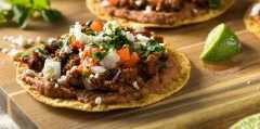 Crispy tostada topped with fresh lettuce, diced tomatoes, avocado slices, and cheese on a rustic surface.