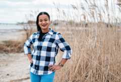 Woman with dark hair, plaid shirt and jeans outside in marshy area.