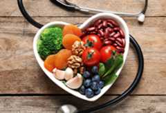 Heart-shaped bowl filled with fruits and vegetables surrounded by a stethoscope.