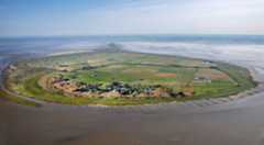 Arial photograph of Mondoe, a flat green island surrounded by sea.