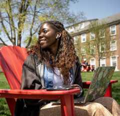 A students sits outside on the quad with her laptop