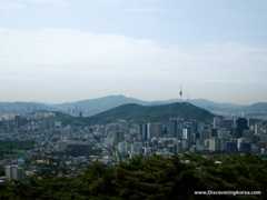 View over Seoul with the tower in the center of the frame, mountains in the background and cityscape.