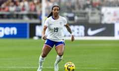A player in a white and blue US national team jersey dribbles the ball on a soccer field