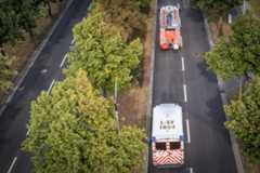 Blick von oben auf ein Löschfahrzeug und einen Rettungswagen, die hintereinander eine doppelspurige Schnellstraße entlang fahren. Links und Rechts der Straße stehen Bäume.