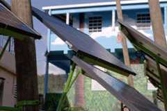 Several solar panels angled upwards, with a blue building featuring a mural of trees and a butterfly in the background.