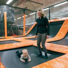 A woman stands on padded trampolines at an indoor play centre in a Finnish civil defencive shelter while her baby crawls nearby.