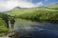 Angler casting on river with mountains in background