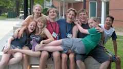 A group of eight Quakers seated on a bench, with one laying across the laps of the rest.